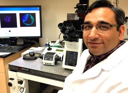 an in white lab coat faces camera while seated at lab bench, equipment on lab benchtop