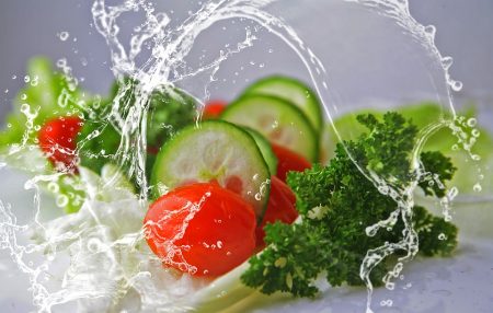 cucumbers, tomatoes and leafy greens being splashed with water