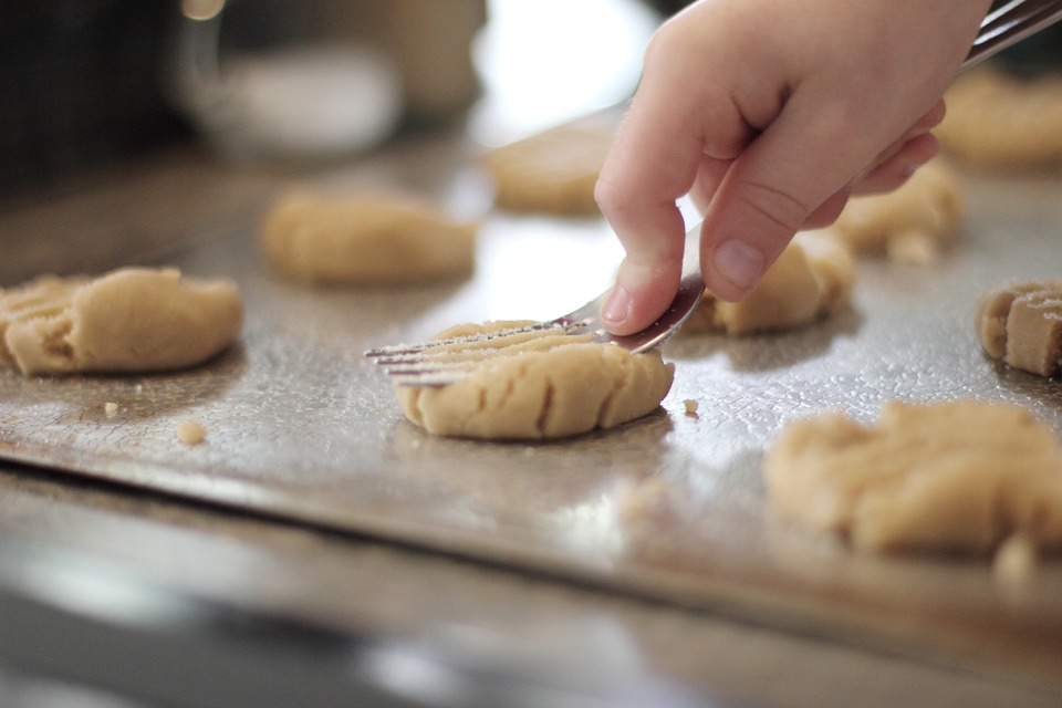 kids hand pressing down cookie dough on cookie sheet