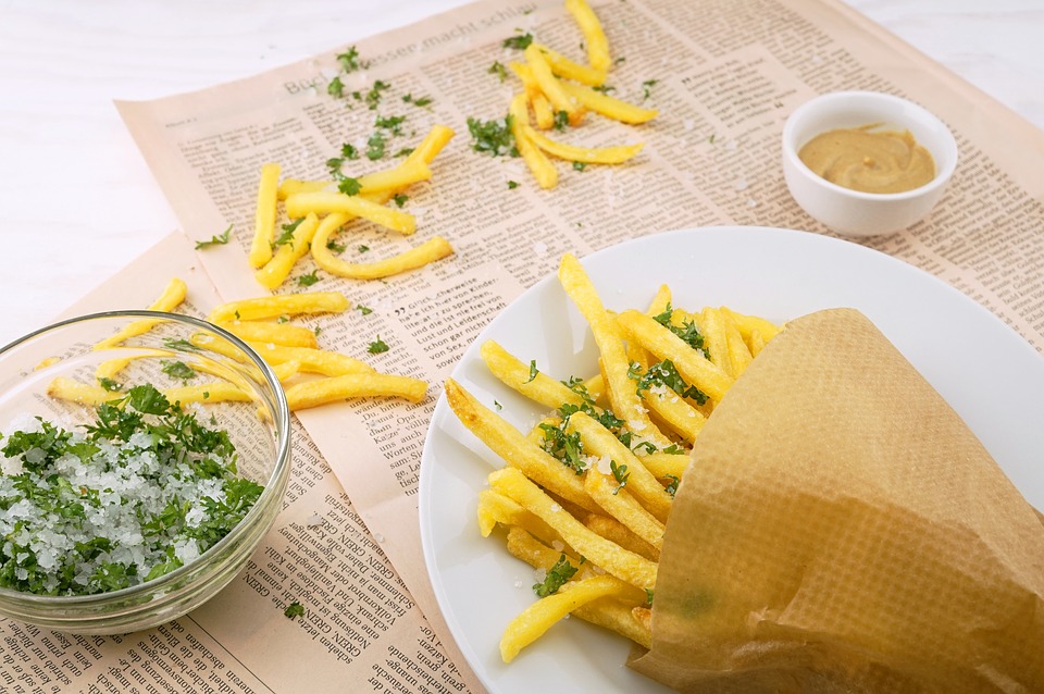 french fries falling out of paper cone onto plate and newspaper resting on table