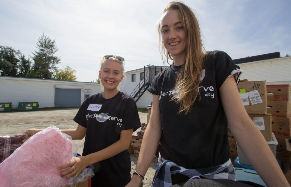 two female students volunteering at the Guelph food bank, lifting boxes, smiling to camera