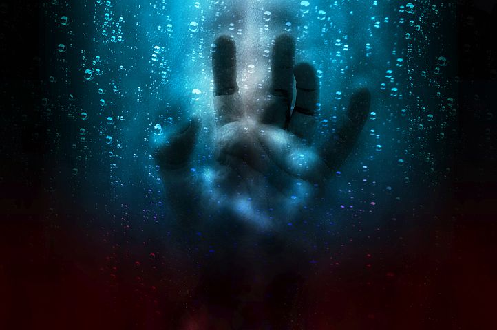 image of a hand pushed against glass surrounded by water, with a faded face in the background