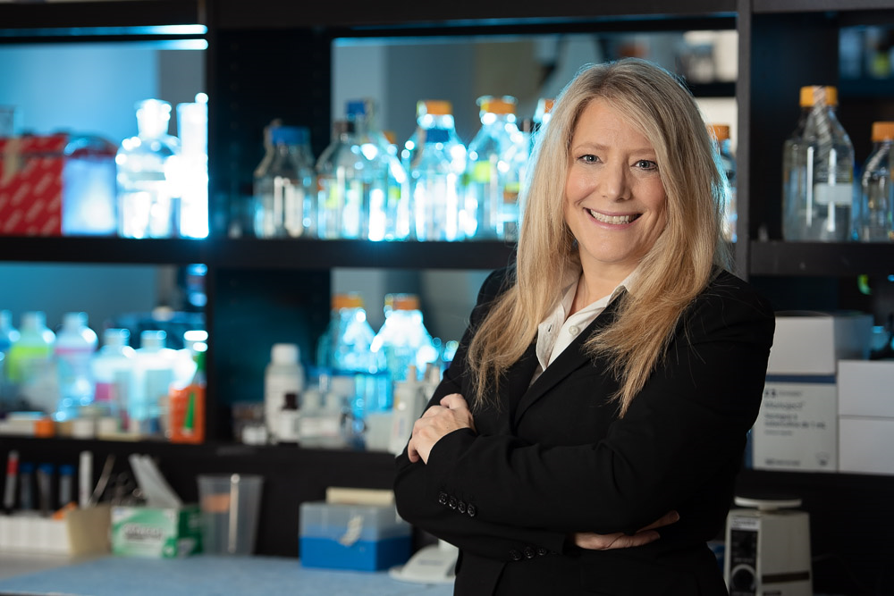 photo of Prof. Tami Martino standing in front of lit up lab bottles