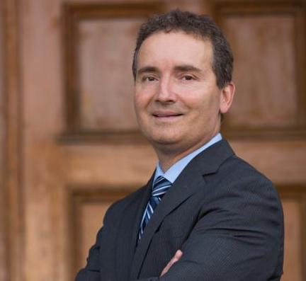 Dr. Rene Van Acker stands in front of a wood-panelled wall
