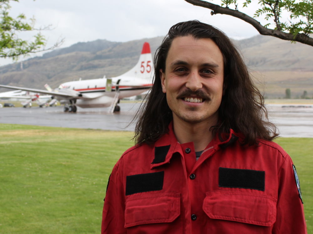 Man with long hair and moustache outdoors along an air strip