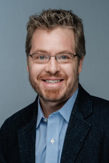 Dr. Tim Dewhirst poses for a headshot against a blue-grey backdrop.
