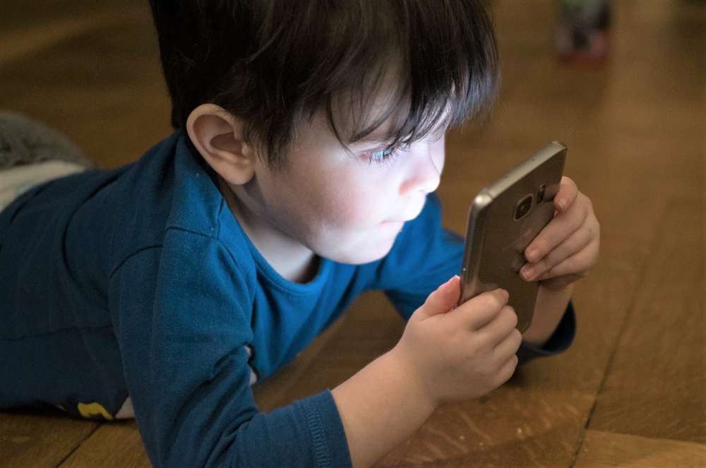 A preschooler smiles while looking at a smartphone