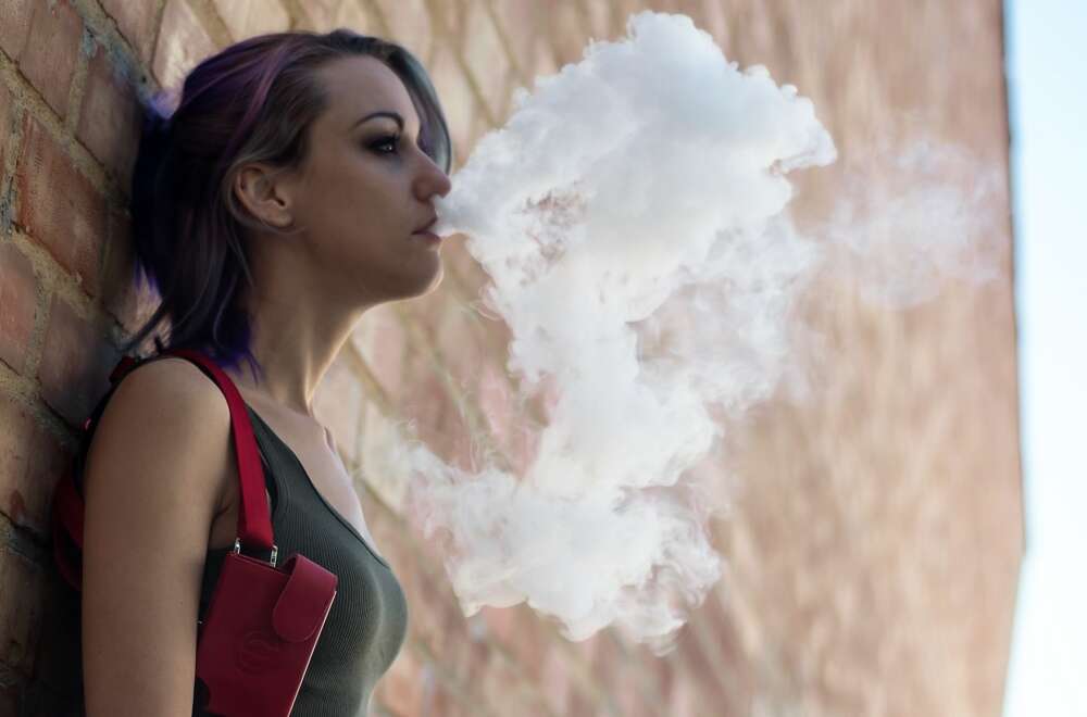 A teen girl blows out vape steam