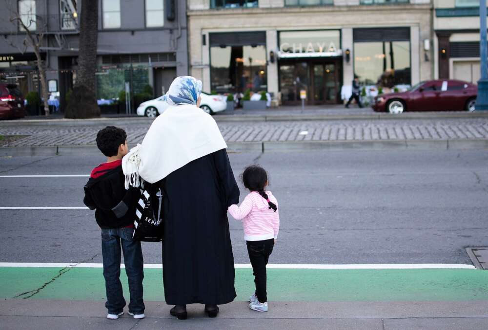 A mother stands with 2 children waiting to cross a street