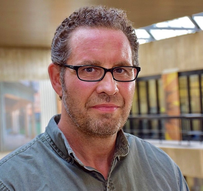 Dr. Andy Hathaway poses for a headshot in front of yellow brick walls and windows.