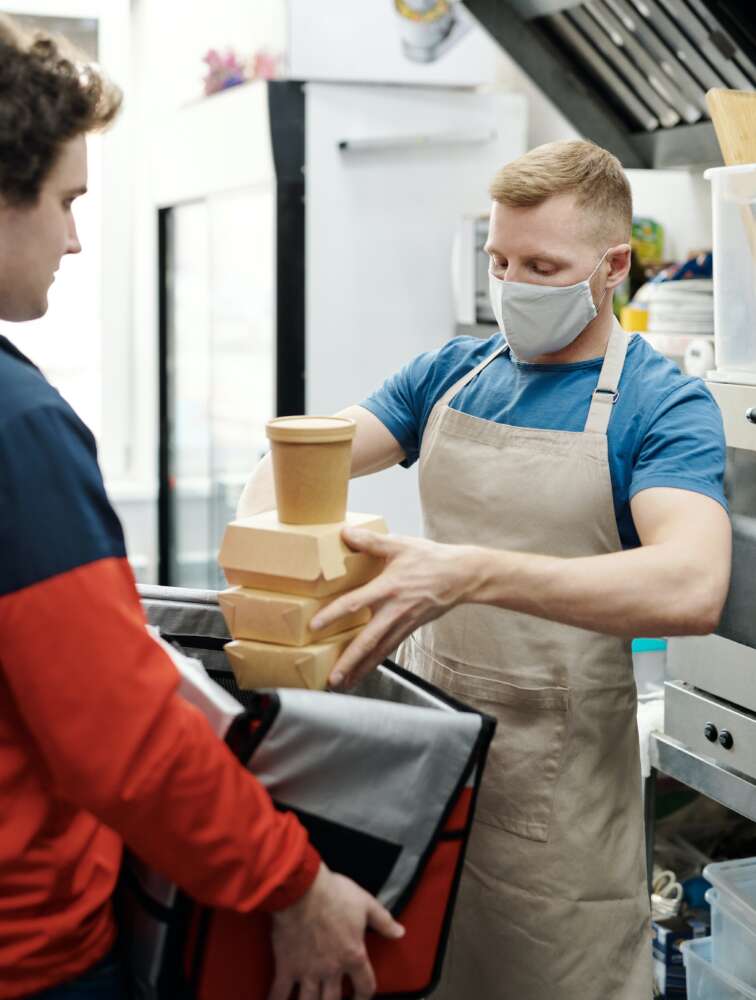 A cook loads takeout boxes into an insulated delivery bag