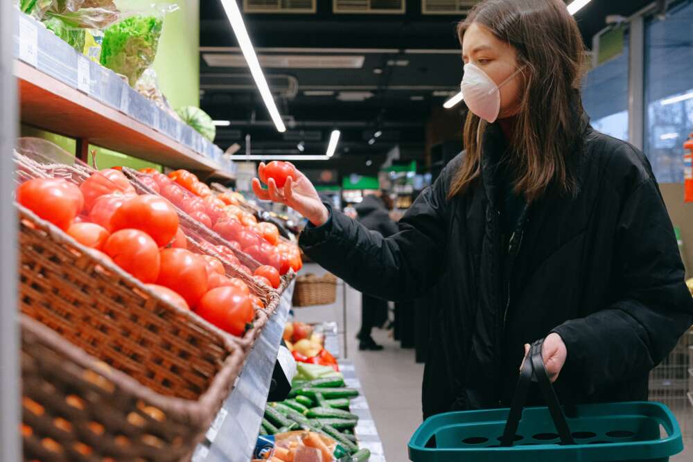 A woman wearing a face mask checks tomatoes in a grocery aisle