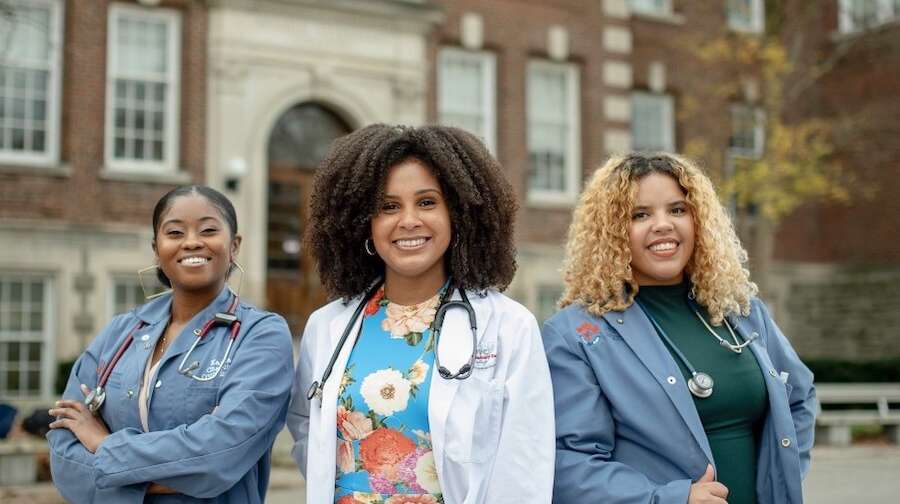 Three Black women in front of OVC building, each wearing a stethoscope