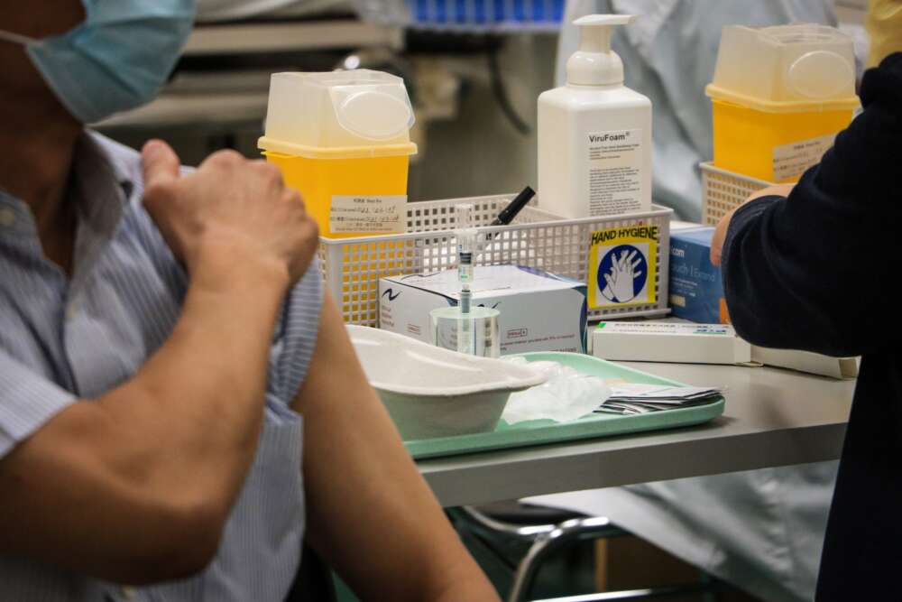 A person wearing a mask rolls up their sleeve at a vaccine clinic