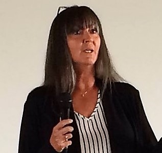Dr. Myrna Dawson speaks at an event, while standing in front of a beige wall.