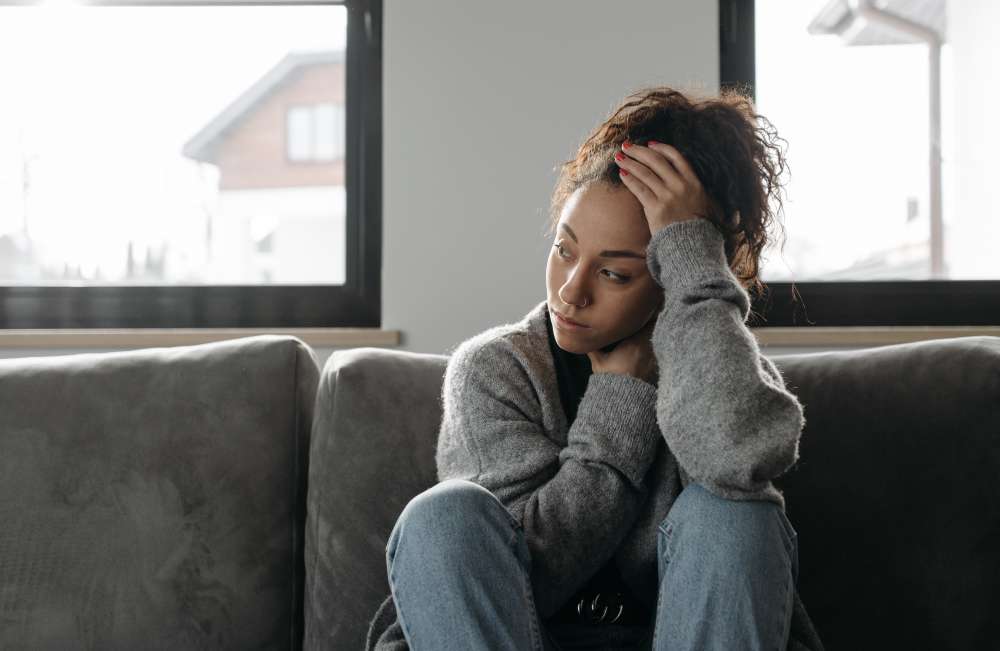 A woman holds her head and throat while sitting on a sofa