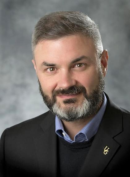 Dr. Stuart McCook poses in suit jacket in front of grey background.