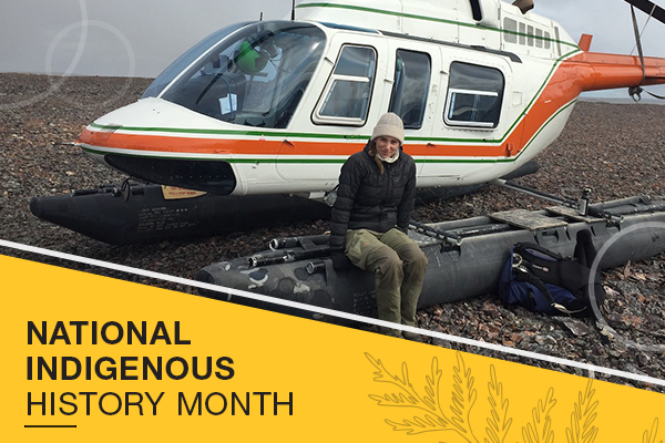A woman sits in front of a helicopter in a tundra region
