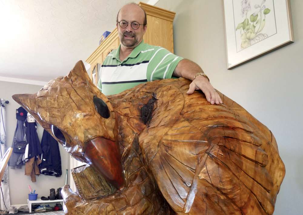 Man standing behind a large wooden gryphon carving