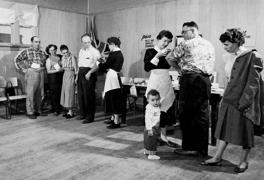 A black and white photo of . Two public health nurses vaccinating adults at a polio clinic.