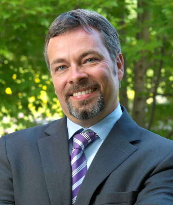Prof. Bruce McAdams poses for a headshot in front of trees.