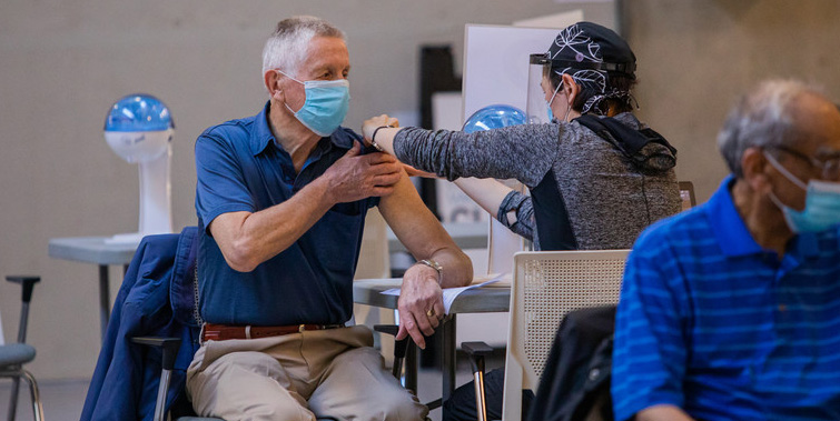 A man wearing a mask is given a needle at a vaccination clinic