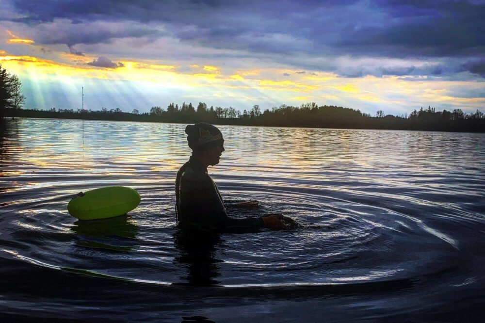 A silhouette of a woman in a swimcap in a lake with a sunset behind her