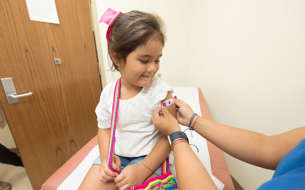 A young girl smiles as a health care workers applies a bandage to her shoulder after a vaccination