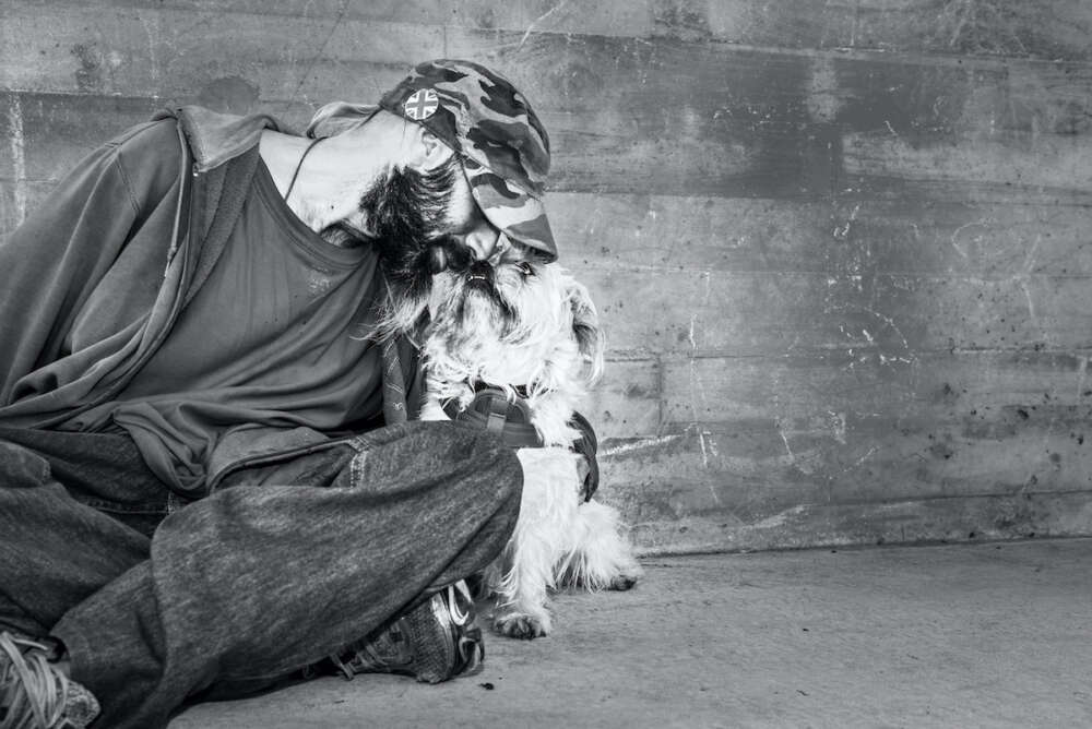 A man and his dog sitting against a concrete wall