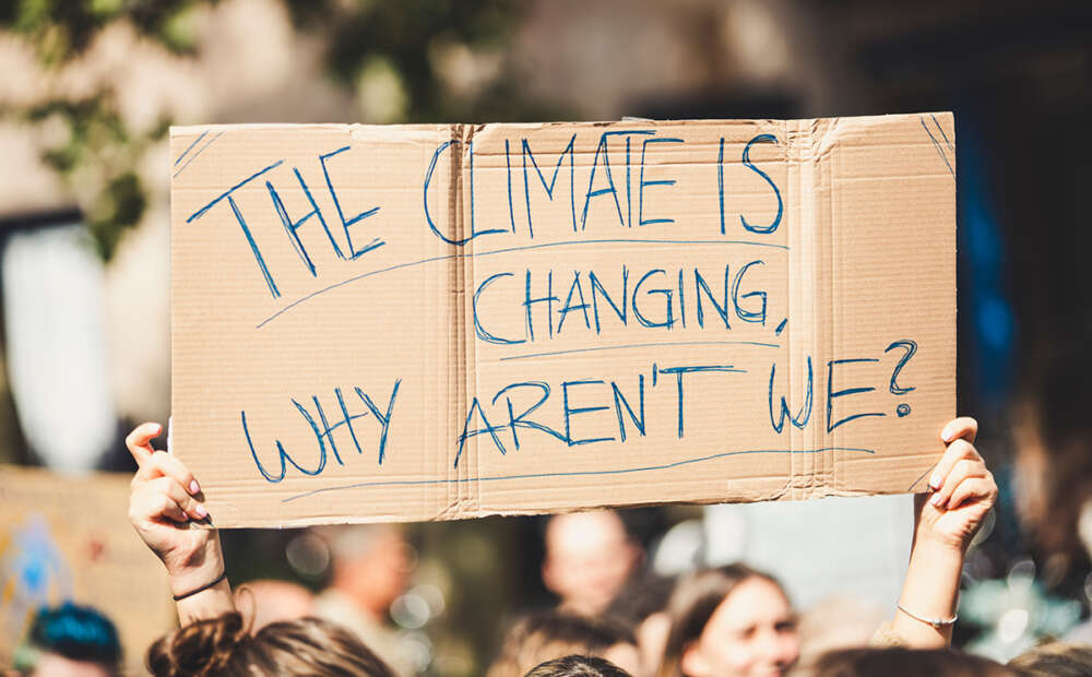 A protest sign is held up that reads "The climate is changing. Why aren't we?"