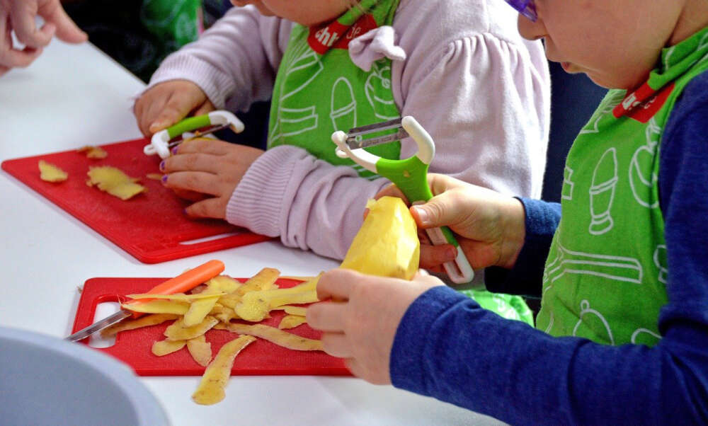 Two young children wear aprons and peel potatoes on