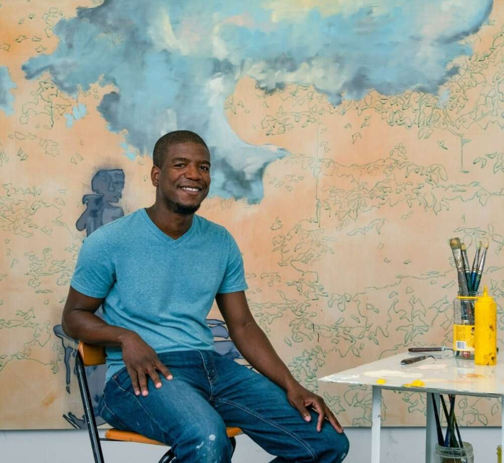Plaskett award winner Emmanuel Osahor sits in front of a large canvas of his work