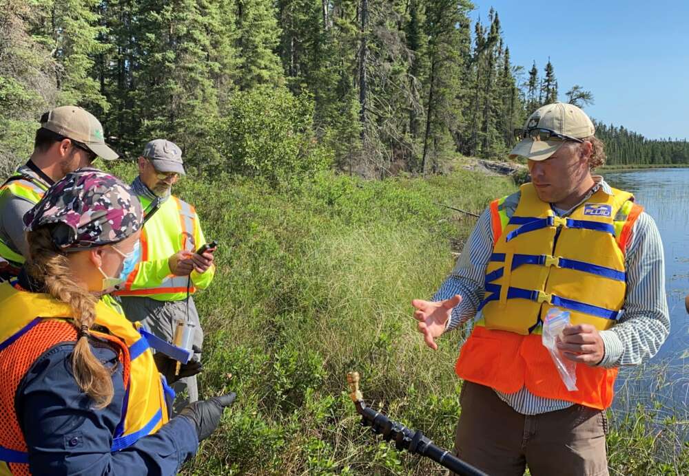 Four people on lakeshore against foliage