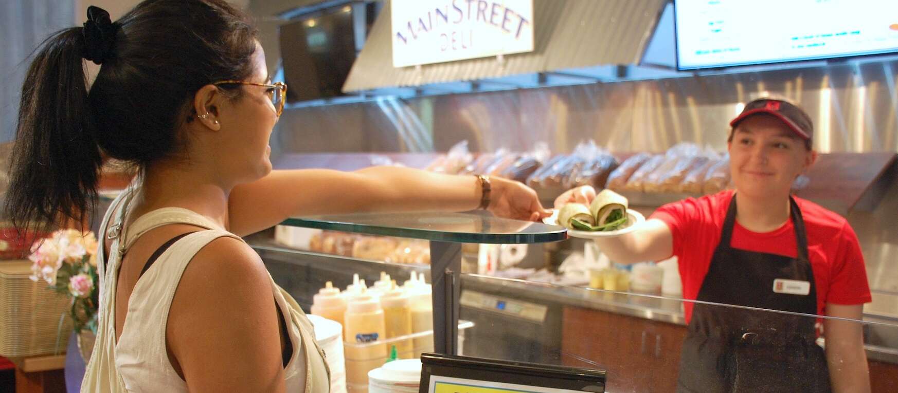 A woman at a sandwich bar takes a wrap from an employee