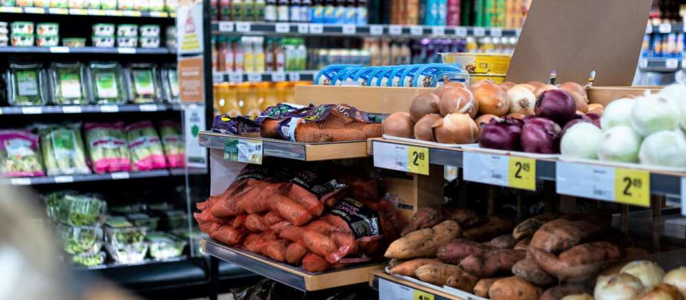 Onions and sweet potatoes are displayed in a grocery store produce area