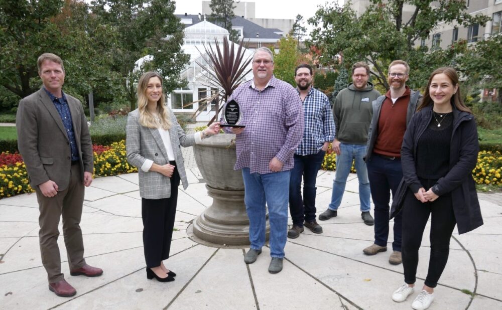 A woman passes a trophy to six people in the gardens on the U of G campus