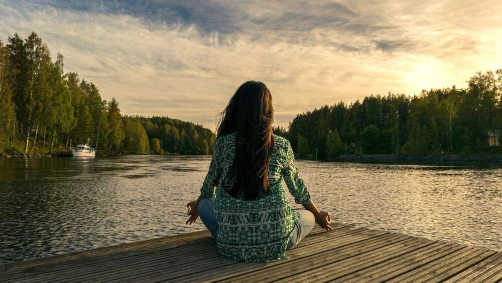 A woman sitting crosslegged on a dock is shown from behind
