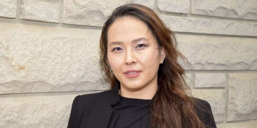 A woman stands against a stone wall