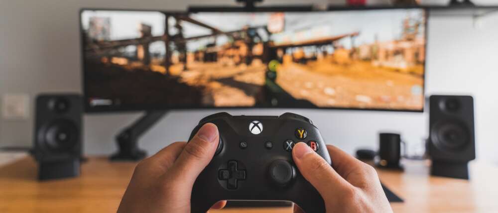 hands hold a gaming console in front of a TV