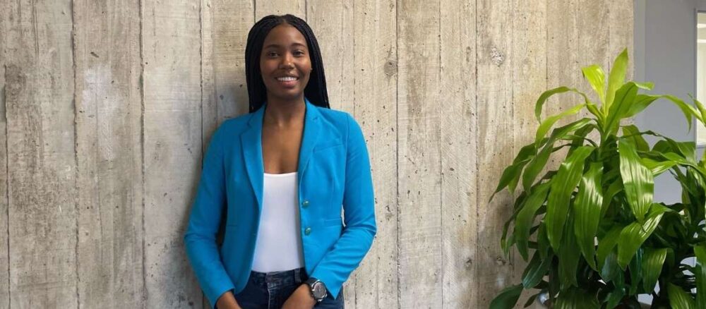 A woman smiles while standing before a concrete wall
