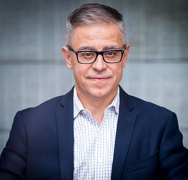Dr. George Bragues poses for a headshot against a blue-grey wall.