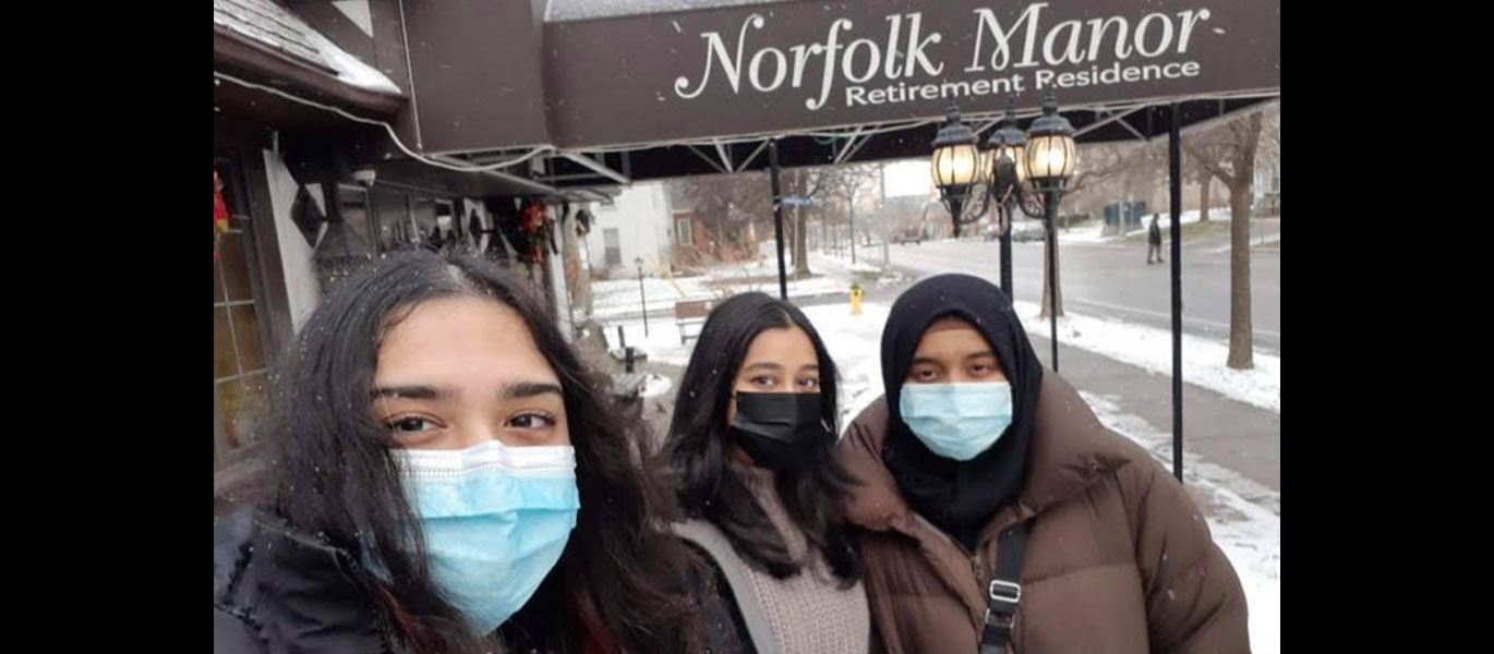 Three students wearing masks pose for a selfie outside of Norfolk Manor Retirement Residence