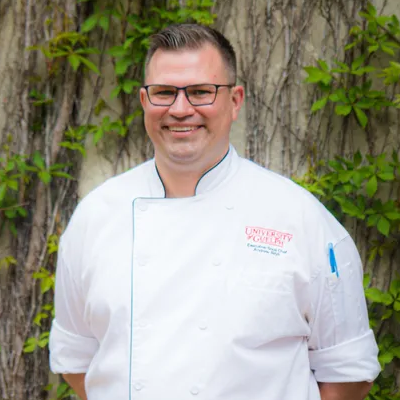 Andrew Bilyk poses in front of a concrete wall with plants.