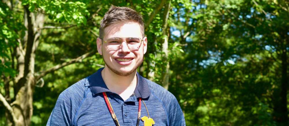 Brad Howie stands in a blue shirt against a background of trees at The Arboretum.