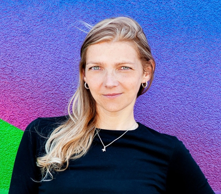 Dr. Susan Dupej poses for a headshot against a green, pink, purple and blue wall.