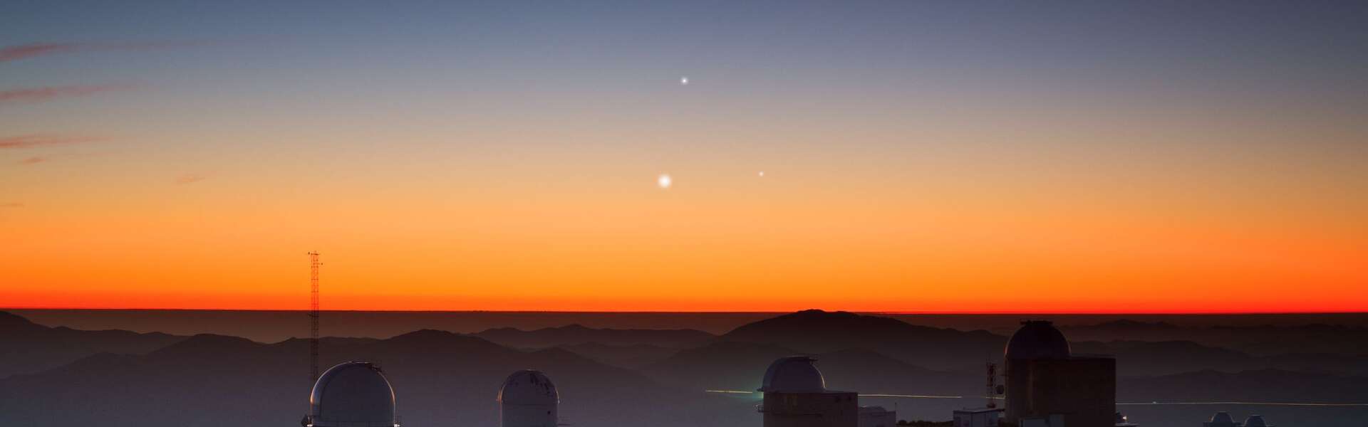 A bright orange sunrise over SO's La Silla Observatory in northern Chile. In the centre of the sky are three shiny lights: Jupiter (top), Venus (lower left), and Mercury (lower right) forming a triangle.