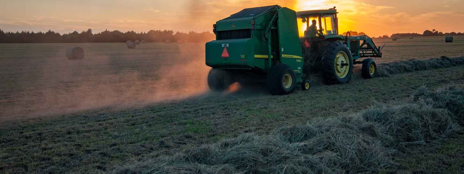 Farm equipmentstirs up dust on a field during sunset
