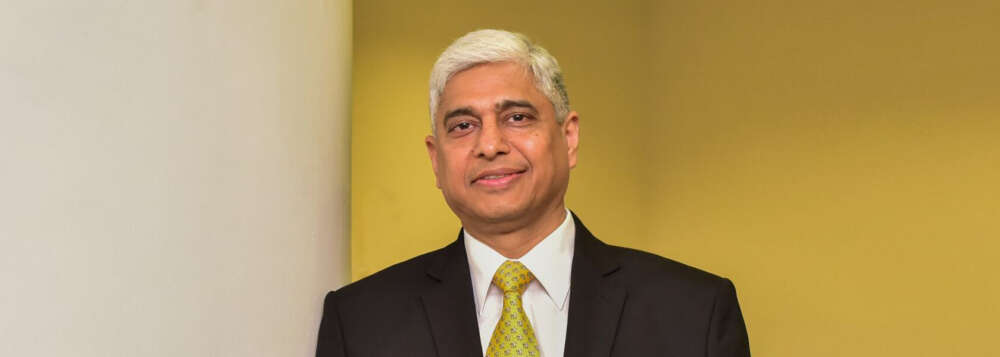 Vikas Swarup wears a yellow tie and stands against a yellow wall