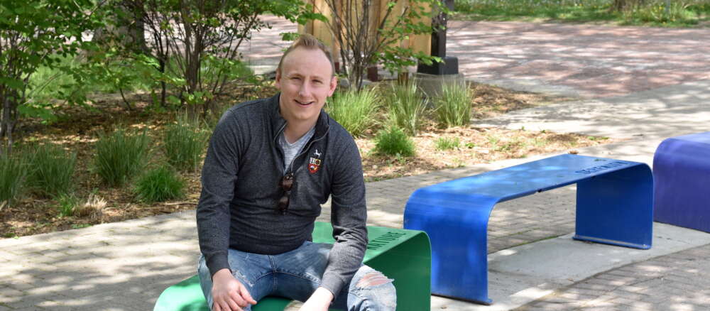 Dr. Adam Davies sits on rainbow-coloured benches at U of G