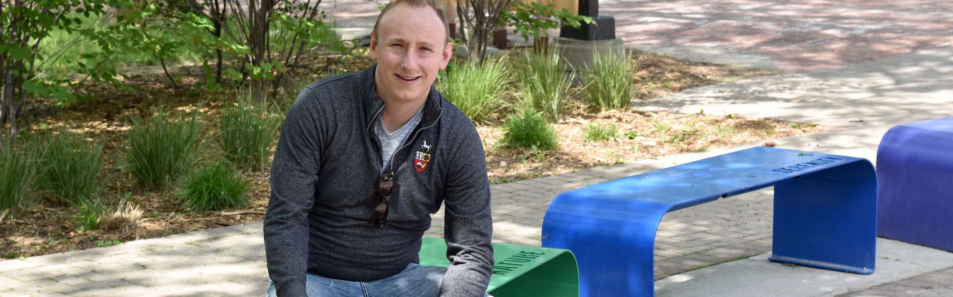 Dr. Adam Davies sits on rainbow-coloured benches at U of G